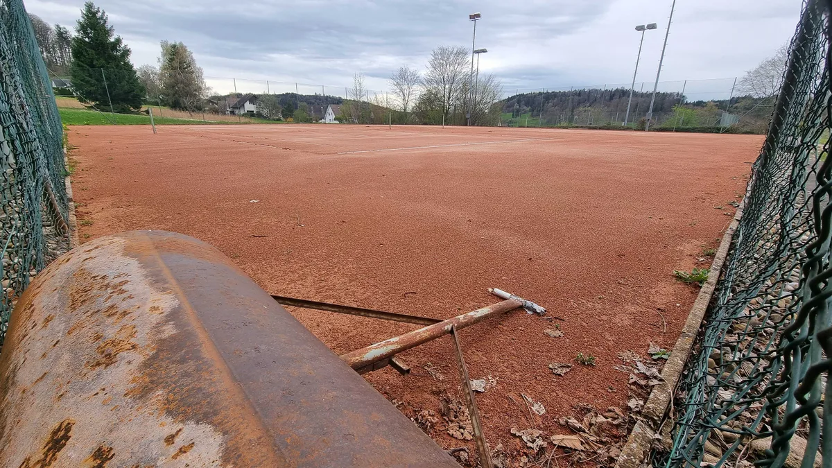 Eine rostige Platzrolle steht auf einem rötlichen Sandtennisplatz. 